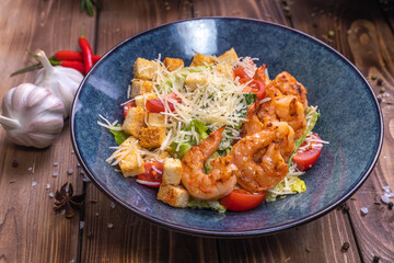Salad with shrimps, grated cheese, tomatoes, crackers, lettuce leaves on a wooden background.
