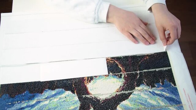 woman removes the protective coating and shows the adhesive base for collecting diamond embroidery. break for creativity and hobbies