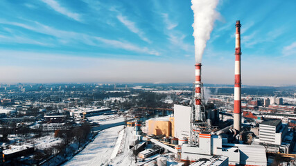 Elevated view of city in winter. Two red and white striped chimneys in a factory at the riverbank. White smoke. 