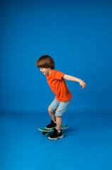 Fototapeta na wymiar playful boy with brown hair rides a skateboard on a blue background with a place for text