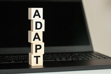 adapt word made with building blocks on the black keyboard. A row of wooden cubes with a word...