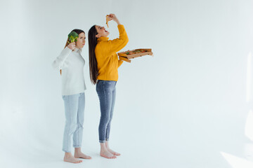 Two young woman choosing between broccoli or pizza. Healthy clean detox eating concept. Vegetarian, vegan, raw concept. Copy space.