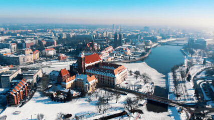 High angle view on winter snowy town, Wroclaw, Poland. Red roofs of sacral buildings and church on sand island. 