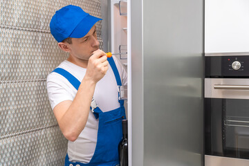 Uniformed repairman repairs the refrigerator door in the kitchen