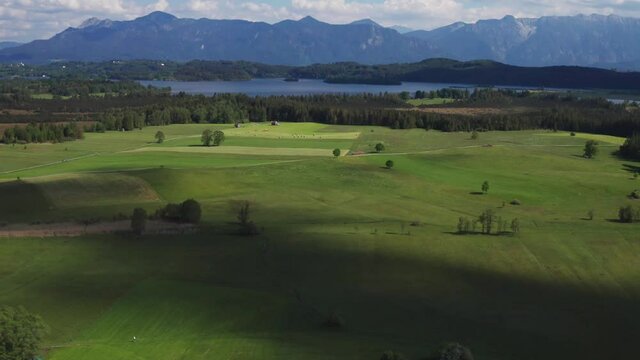 Lake Staffelsee in Bavaria with Alp mountains during summer, blue sky with clouds, green fields, drone view, reveal moving forward
