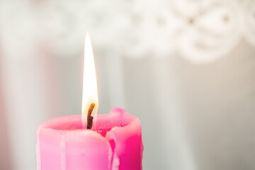 one thick pink candle lit on a light background.