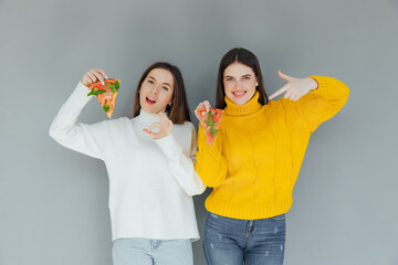 Pizza time. Handsome smiling women eating pizza, having fun together on gray background. Consumerism, food, lifestyle concept