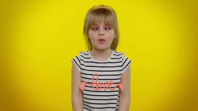 Cute funny teen child kid girl making playful silly facial expressions and grimacing, fooling around, showing tongue. Posing isolated on yellow studio background. Childhood lifestyle. Young children