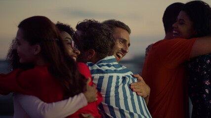 Cheerful people hugging at evening party. Buddies greeting each other outdoors. 