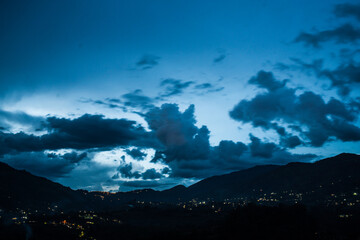 City in the mountains with a cloudy and blue sky at night, from afar. 
