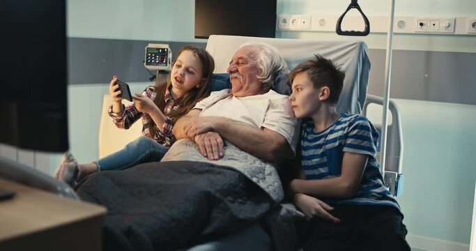 Senior patient discussing video on smartphone with grandchildren in hospital ward