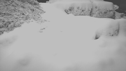 Black and white abstraction of a snowdrift made of snow. White freshly fallen snow covers a large snowdrift with an even clean layer. In the distance, gray-white snow collected from the road.