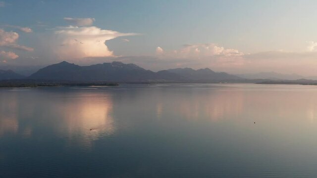 Lake Chiemsee in Bavaria with the Alp mountains during sunset from above, coast near village Chieming, during summer, flying downwards
