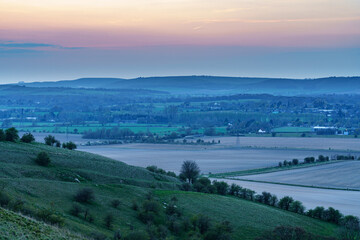a scenic landscape view across Pewsey and Pewsey Vale with sunset illuminating a colourful evening sky in Wiltshire, North Wessex Downs AONB