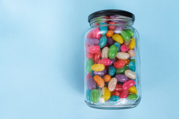 Several Jelly Beans on the blue background inside the glass pot