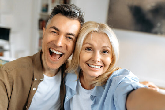 Portrait of beautiful cheerful marriage mature couple in casual clothes, Caucasian husband and wife taking selfie on smartphone, having fun together, looking at camera, smiling