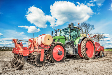 Large, green, modern tractor from Germany sowing potatoes in the field on a sunny spring day
