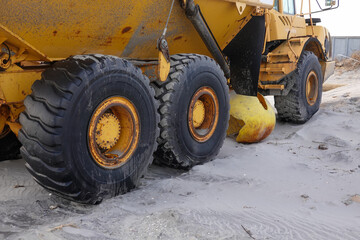 Fototapeta na wymiar Large heavy duty tires on a large yellow construction vehicle on a sandy beach