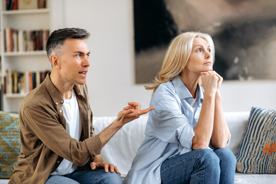 An agitated and upset gray-haired husband shouts and looks at his wife, gestures with his hand, cannot make a decision or compromise, a quarrel between spouses. Family misunderstanding, quarrel