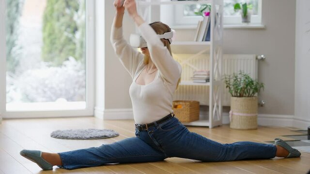 Wide shot of concentrated confident fit woman on twine in VR headset training at home indoors. Slim beautiful Caucasian sportswoman using augmented reality for workout. Sport and modern technologies