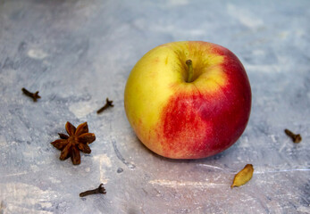 Apple on a silvery-gray background with carnation and star anise. 