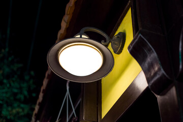 wrought iron wall lamp of round shape and shade with visor on exterior of a building with a yellow...