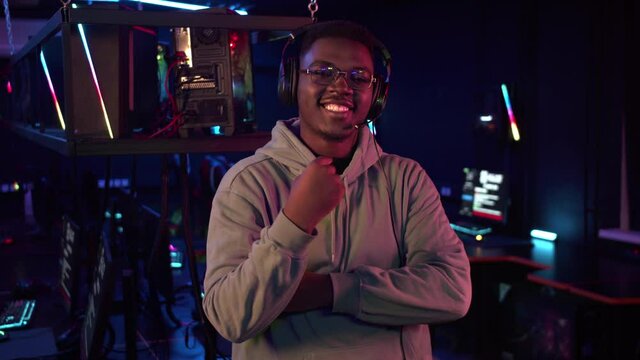 A cute african-american gamer in glasses and headphones beckons with his hand to join him