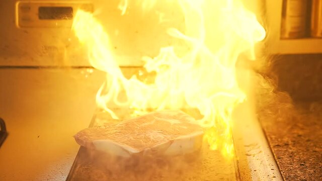 This slow motion video shows a large cut of steak being dropped onto a flaming flat top cooking area.