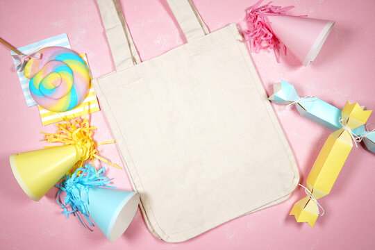 Cottom canvas tote bag. Birthday and parties theme SVG craft product flat lay mock up styled stock photo. Styled with pink, blue and yellow party hats and bon bons on a textured pink background.