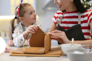 Mother and daughter making gingerbread house at table indoors, closeup