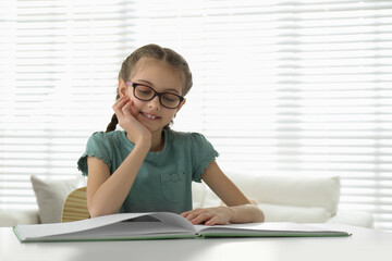 Cute little girl reading book at desk in room. Space for text