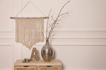 Tree twigs in metal vase and decor on wooden table near white wall. Space for text