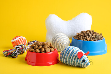 Fototapeta na wymiar Feeding bowls and toys for pet on yellow background