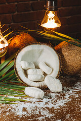 Concept of coconut candy with a ripe half cut coconut with green leaves on a brick wall background