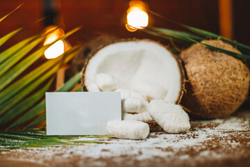 Concept of coconut candy with a ripe half cut coconut with green leaves on a brick wall background