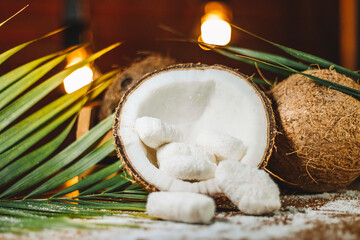 Concept of coconut candy with a ripe half cut coconut with green leaves on a brick wall background