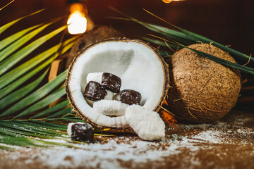 Concept of coconut candy with a ripe half cut coconut with green leaves on a brick wall background