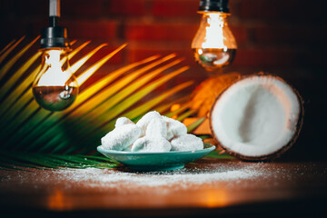 Concept of coconut candy with a ripe half cut coconut with green leaves on a brick wall background