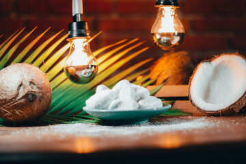 Concept of coconut candy with a ripe half cut coconut with green leaves on a brick wall background