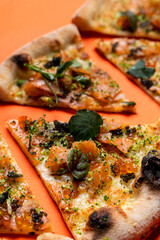 Beautiful appetizing shot of slices of smoked salmon pizza placed in a row, close up on orange background