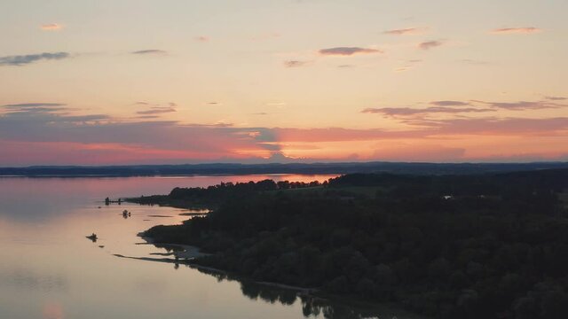 Lake Chiemsee in Bavaria with the Alp mountains during sunset from above, coast near village Chieming, during summer, flying upwards

