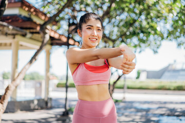 Healthy and fit young Asian woman in sportswear doing warming up stretching exercise with hands before morning run and jog in park