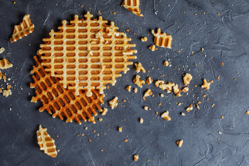 Top view of flat homemade waffles on dark textured background. Vanilla waffles whole and smashed with pastry dragees.