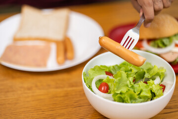 A young man eating breakfast. Breakfast set includes bread, bacon, salad and sausage.