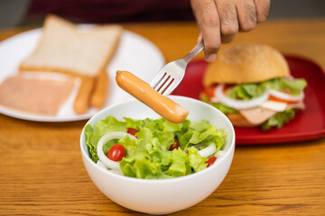 A young man eating breakfast. Breakfast set includes bread, bacon, salad and sausage.