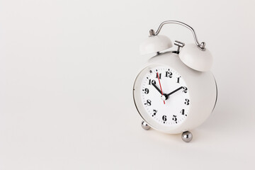 Small white alarm clock, black numbers, set the time for 10.10 o'clock, placed on a white table.