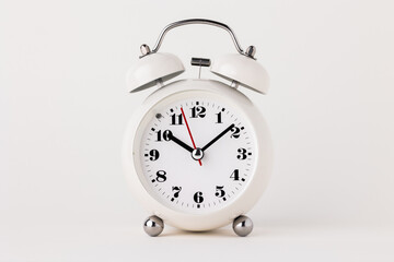 Small white alarm clock, black numbers, set the time for 10.10 o'clock, placed on a white table.