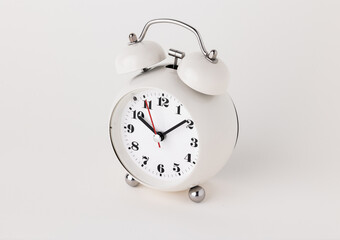 Small white alarm clock, black numbers, set the time for 10.10 o'clock, placed on a white table.