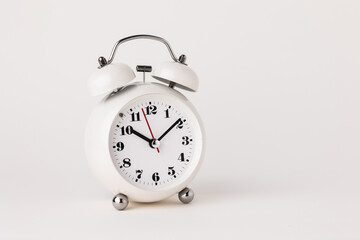 Small white alarm clock, black numbers, set the time for 10.10 o'clock, placed on a white table.