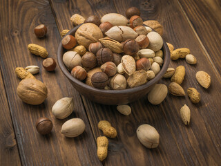 A large number of unpeeled nuts of various varieties on a wooden table.